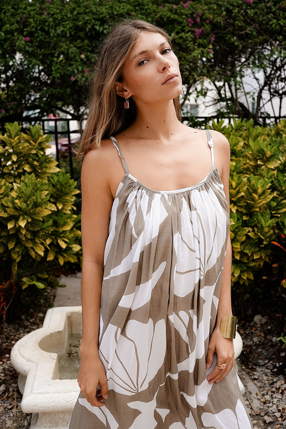 Woman wearing a patterned dress standing outdoors with greenery in the background
