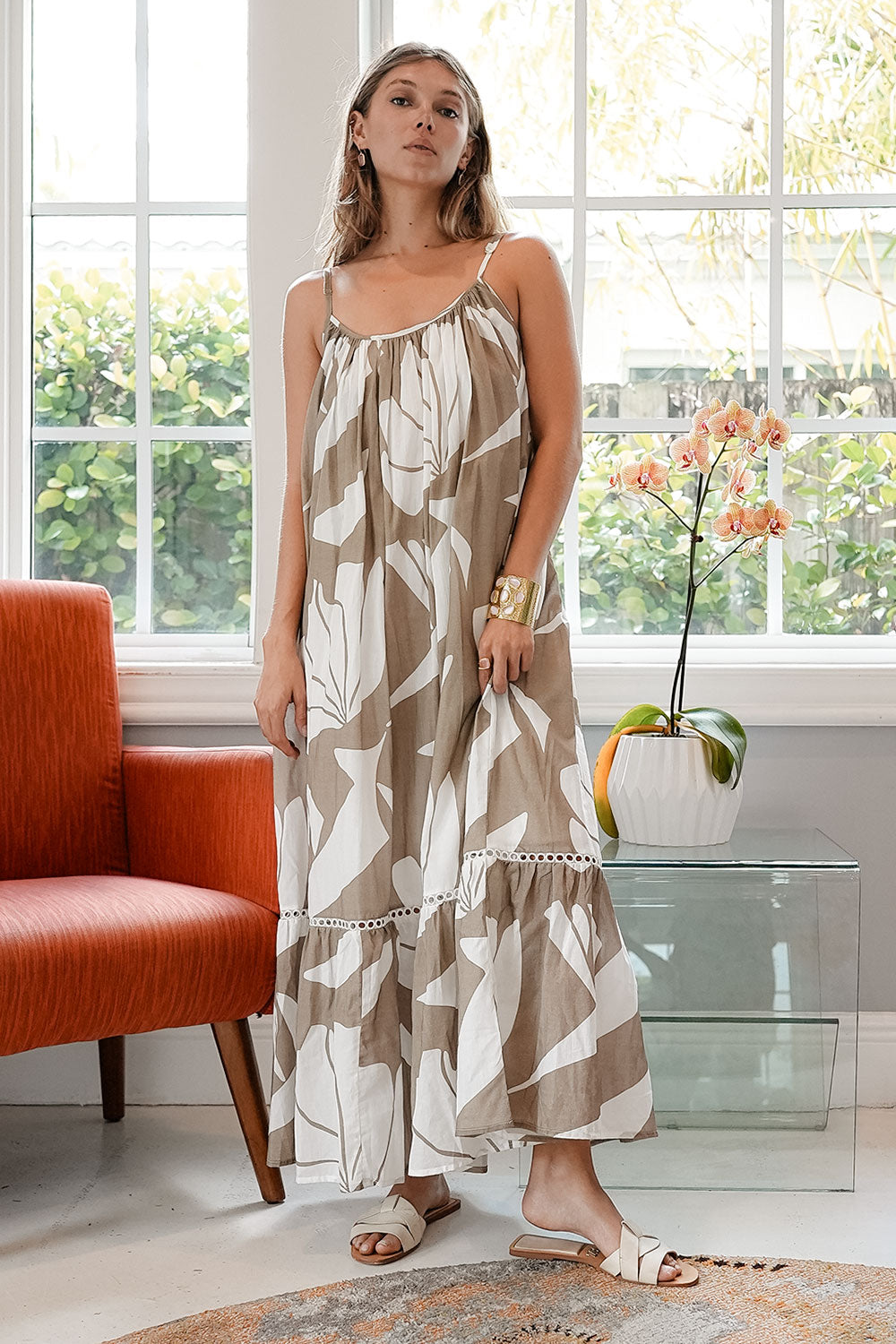 Woman wearing a floral dress in a bright room with large windows.