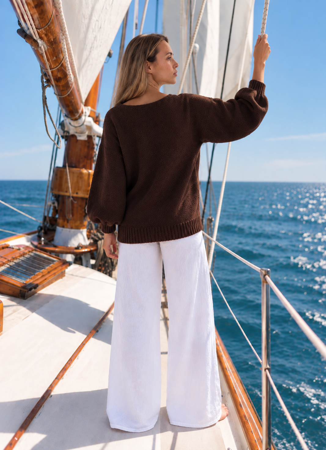 Vail V-Neck Sweater in Chocolate, back view on a sailboat with white trousers.