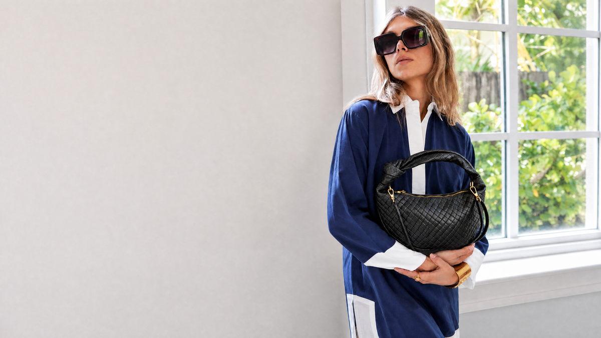 Tonni Black woven bag held with a navy resort dress by a window